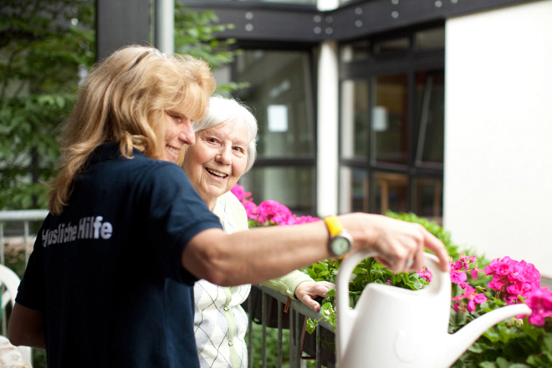 Eine DRK Mitarbeiterin gießt mit Seniorin blumen